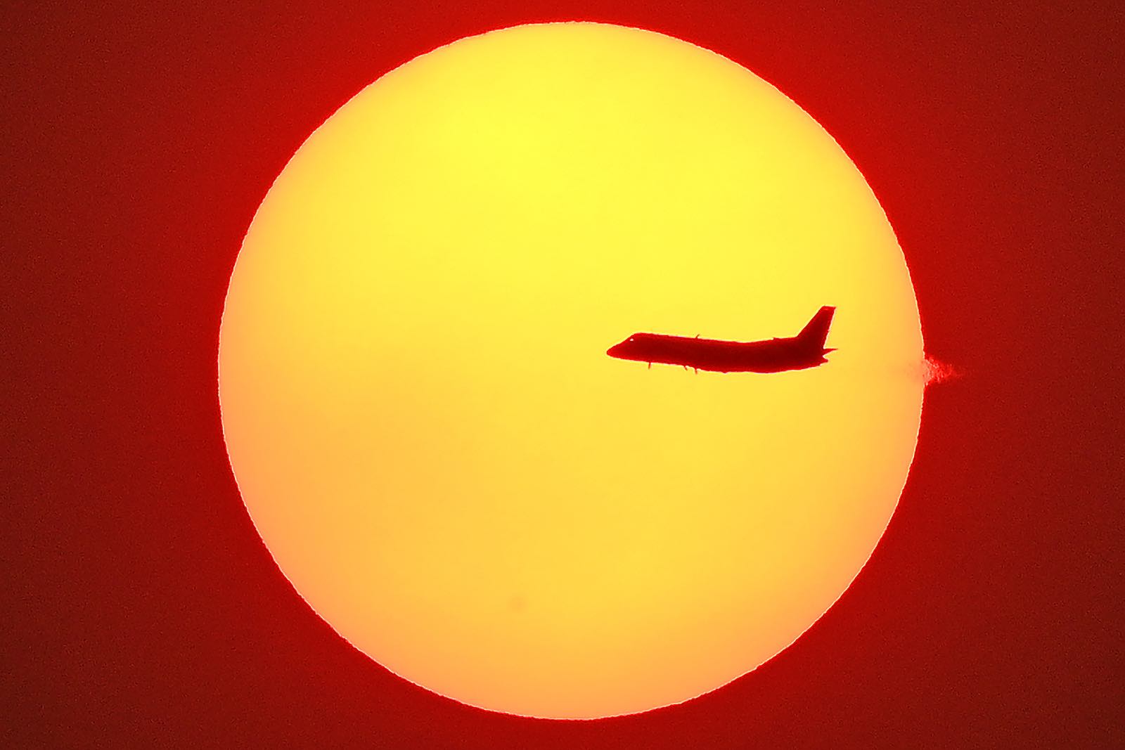 A jet passes in front of a smoke-shrouded sun in Sydney, 4 December 2019 (Photo: Saeed Khan/AFP via Getty Images)