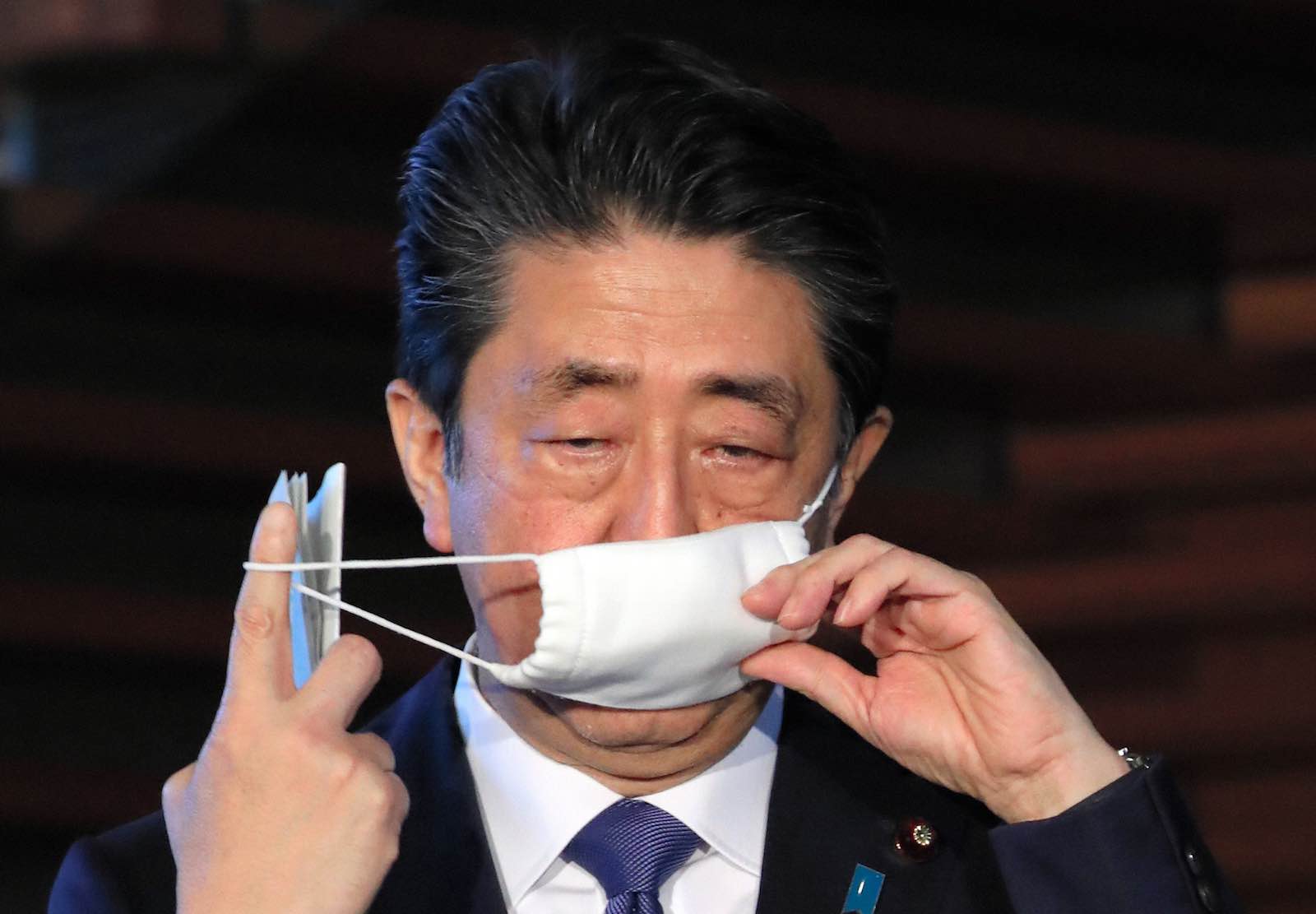 Japan’s Prime Minister Shinzo Abe removes his face mask as he speaks to media reporters prior to the coronavirus task force meeting on 6 April to announce he will declare a state of emergency (The Asahi Shimbun via Getty Images)
