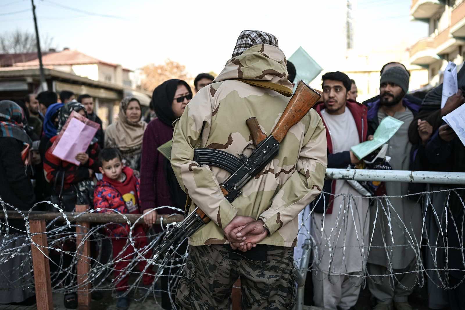 A Taliban fighter stands guard as people queue to enter the passport office at a checkpoint in Kabul this month (Mohd Rasfan/AFP via Getty Images)