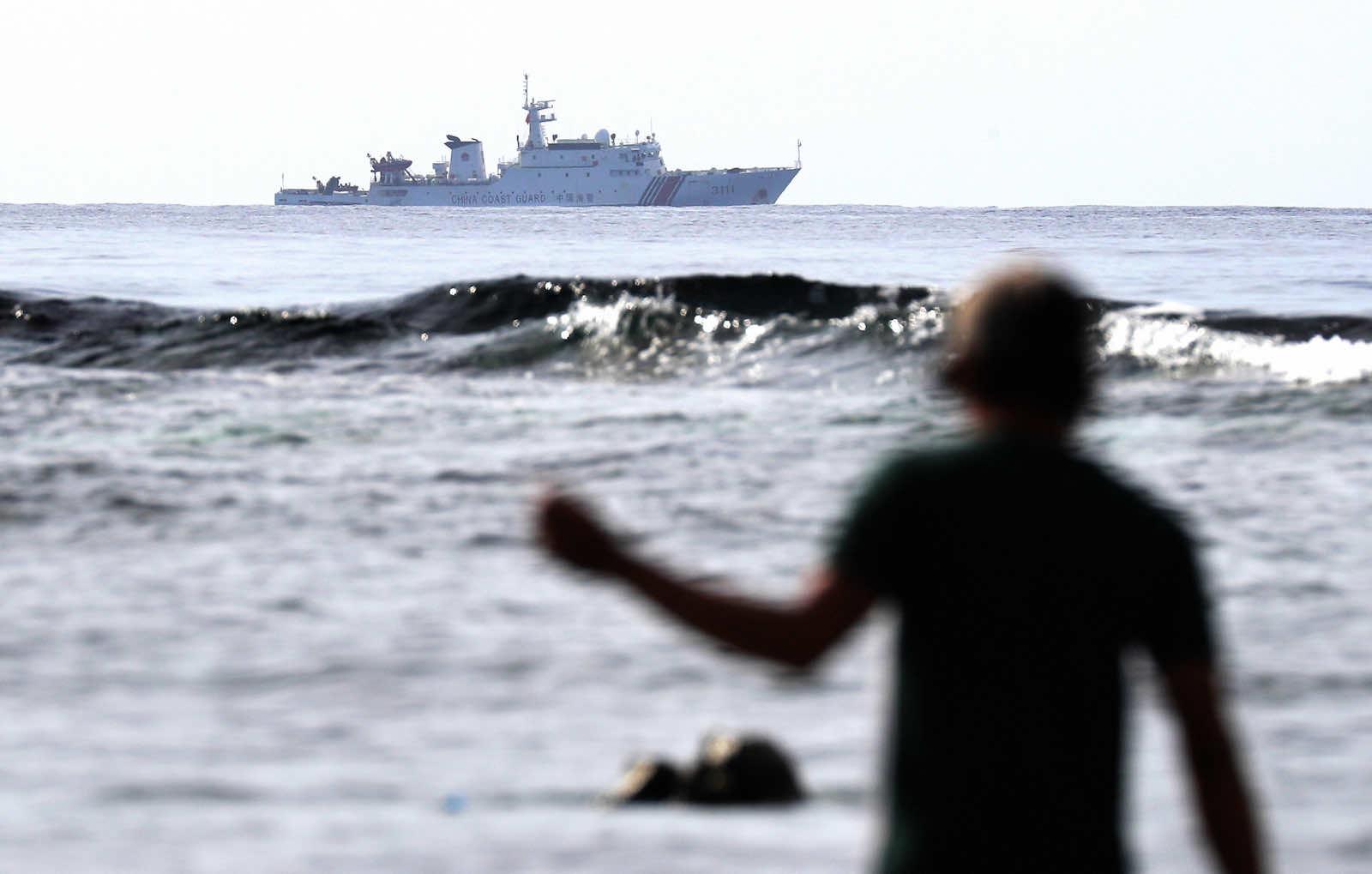 A Filipino fisherman near Scarborough Shoal in 2016 while a Chinese Coast Guard ship sails close by (The Asahi Shimbun via Getty Images)