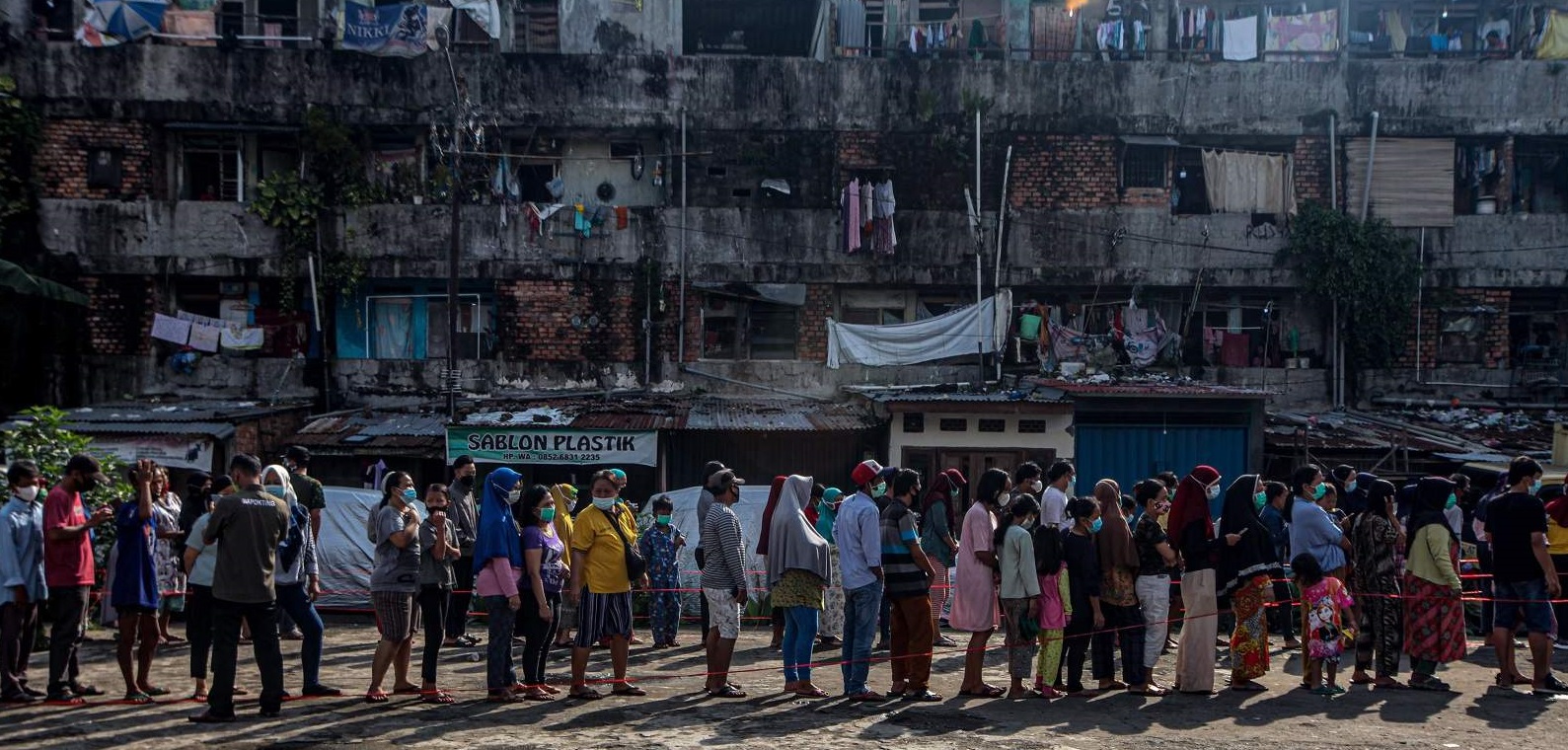Hundreds of people line up for foodstuffs at a slum area in Palembang, Indonesia on 24 February 2022 (Muhammad A.F/Anadolu Agency via Getty Images)