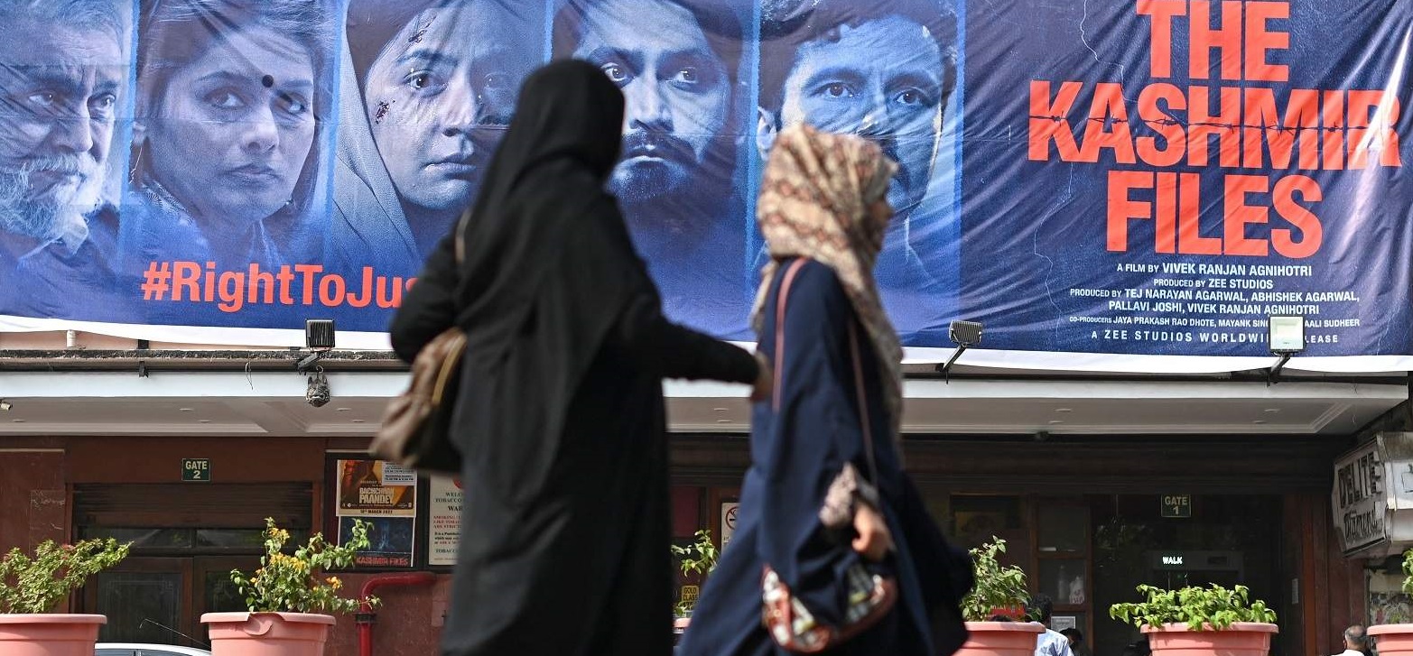 Women walk past a banner advertising “The Kashmir Files” outside a cinema in Delhi on 21 March 2022 (Sajjad Hussain/AFP via Getty Images)
