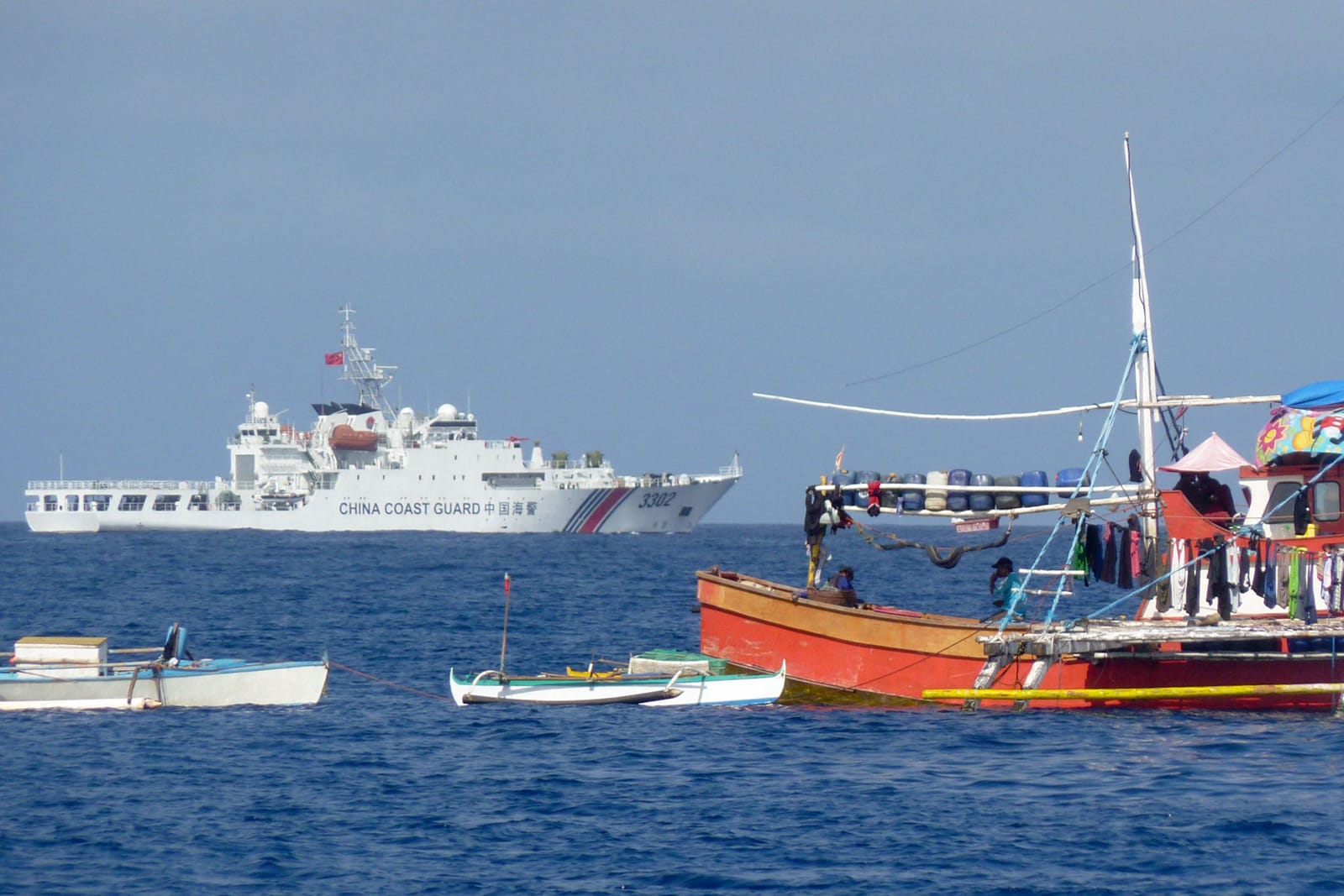 Philippine fishing boats (front) as a Chinese coast guard ship last month sails in the Scarborough Shoal, South China Sea (STR/AFP via Getty Images)