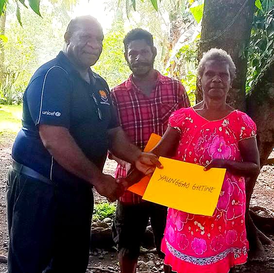 Morobe Province Senior Standards Officer (Secondary Schools) Mr Gibson Wemin Dom presents a certificate to Ms Yaunggao Gietine, teacher at Yawan Elementary School, after a remote learning workshop on Nungon grammar, 2022, as her son Ismael Dono looks on (Author supplied)