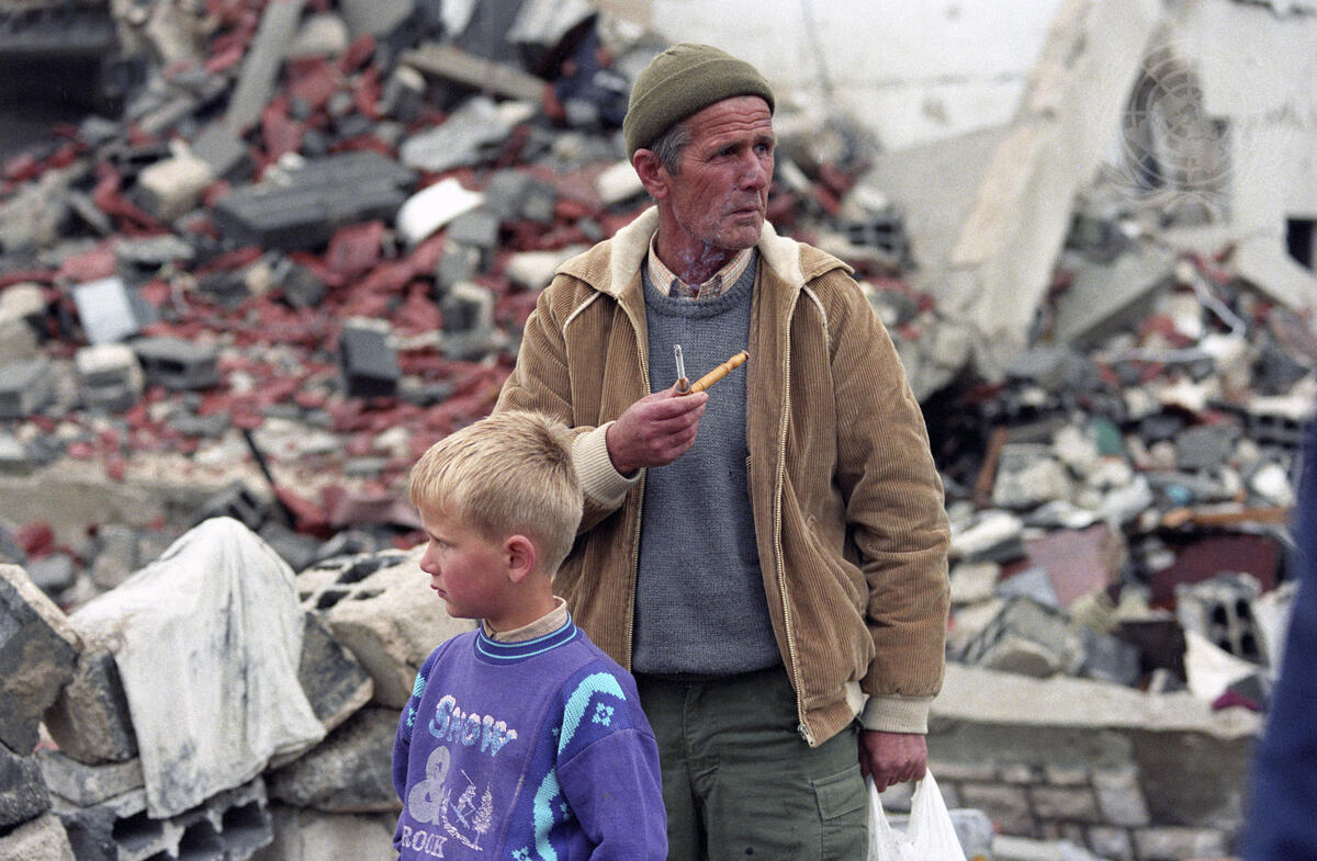 A man with his grandson against a backdrop of the destruction in the Muslim enclave of Stari Vitez (John Isaac/UN Photo)