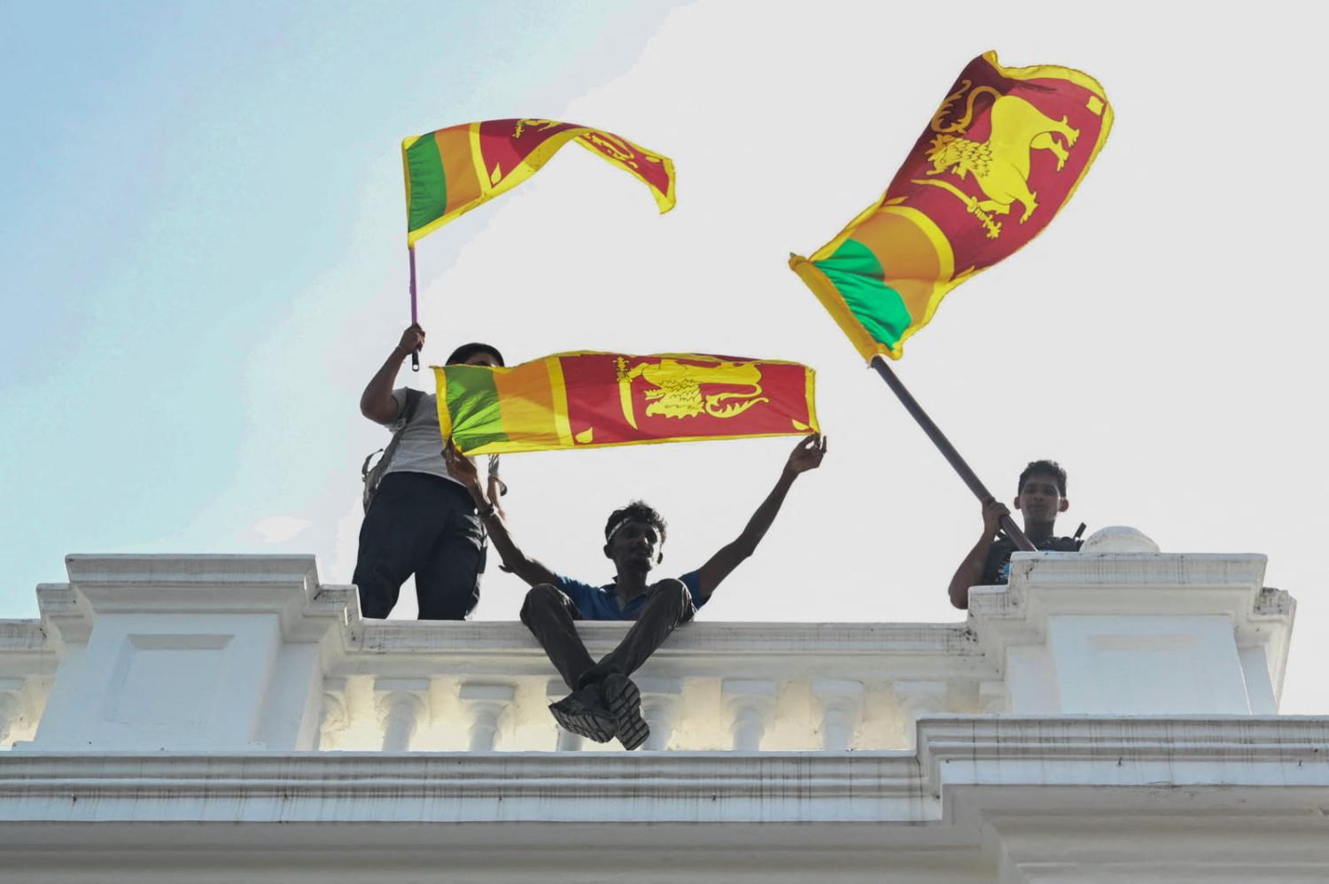 Demonstrators wave Sri Lankan flags from a balcony inside the office building of Sri Lanka's prime minister during an anti-government protest in Colombo on 13 July (Arun Sankar/AFP via Getty Images)