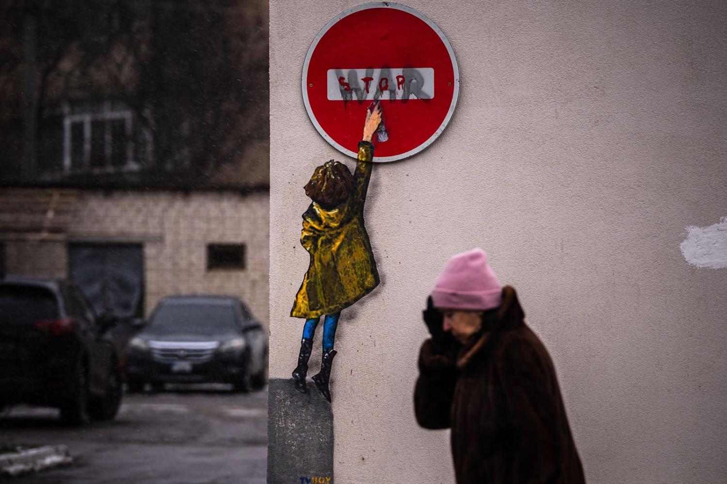A pedestrian passes a mural of Italian urban artist Tvboy on a wall in Bucha amid the Russian invasion of Ukraine, 1 February 2023 (Dimitar Dilkoff/AFP via Getty Images)