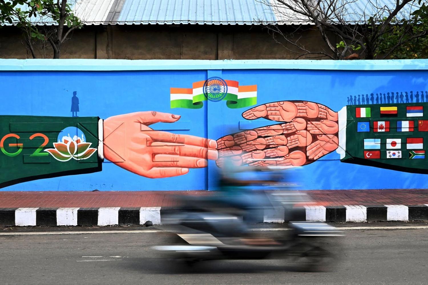 A commuter rides past a G20 Summit mural in Visakhapatnam on 20 March 2023 (Noah Seelam/AFP via Getty Images)