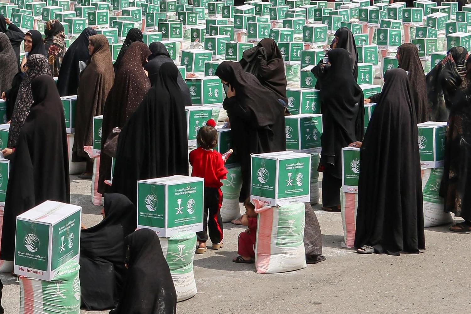 Afghan women gather around aid parcels containing food items distributed by the King Salman Humanitarian Aid and Relief Centre in Herat on 21 June 2023 (Mohsen Karimi/AFP via Getty Images)