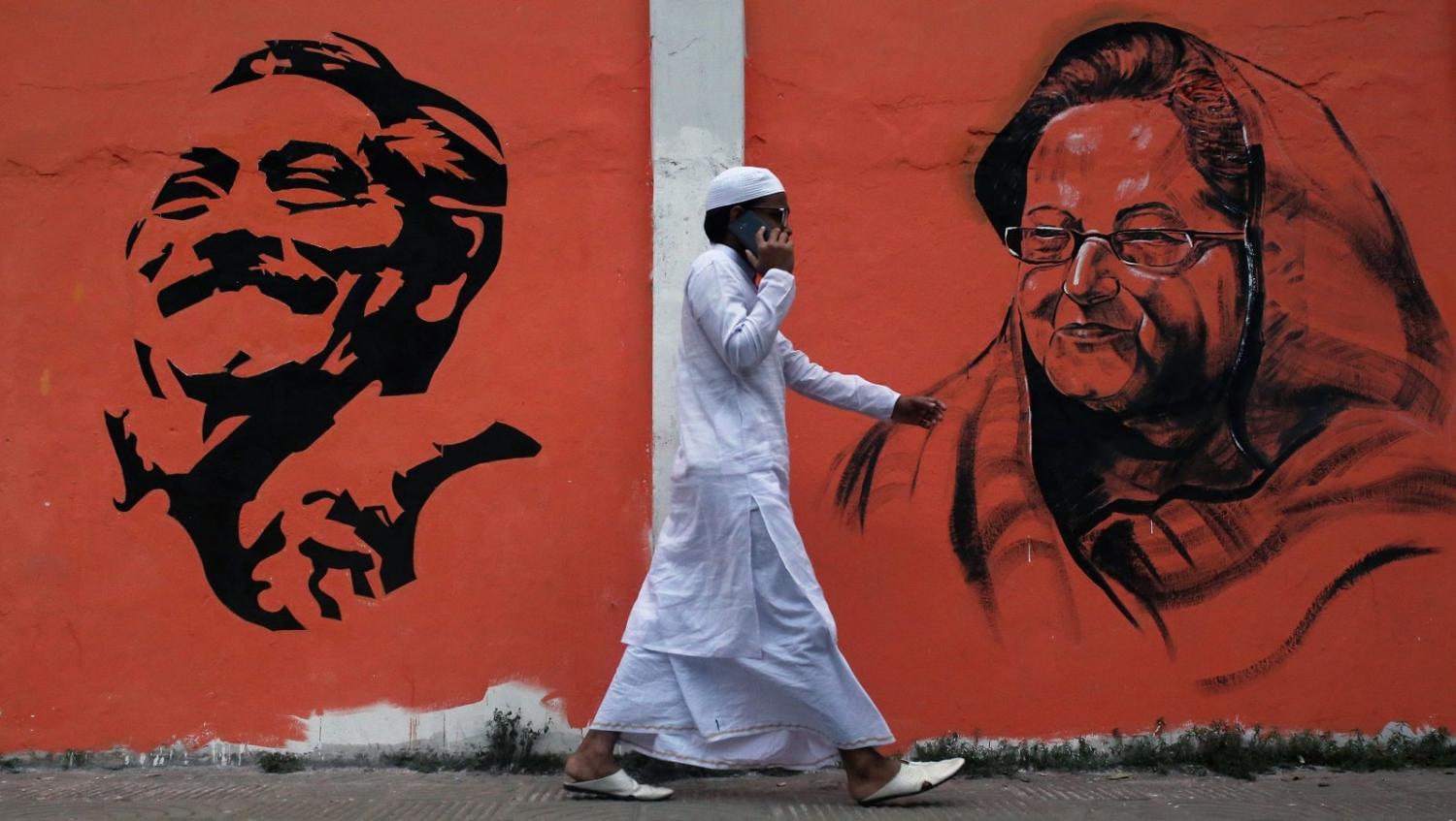 A man walks past a wall with images of Bangladeshi founding father Sheikh Mujibur Rahman (L) and Prime Minister Sheikh Hasina Wazed (R) as 2018 general election campaigns take place in Dhaka (Rehman Asad/AFP via Getty Images)