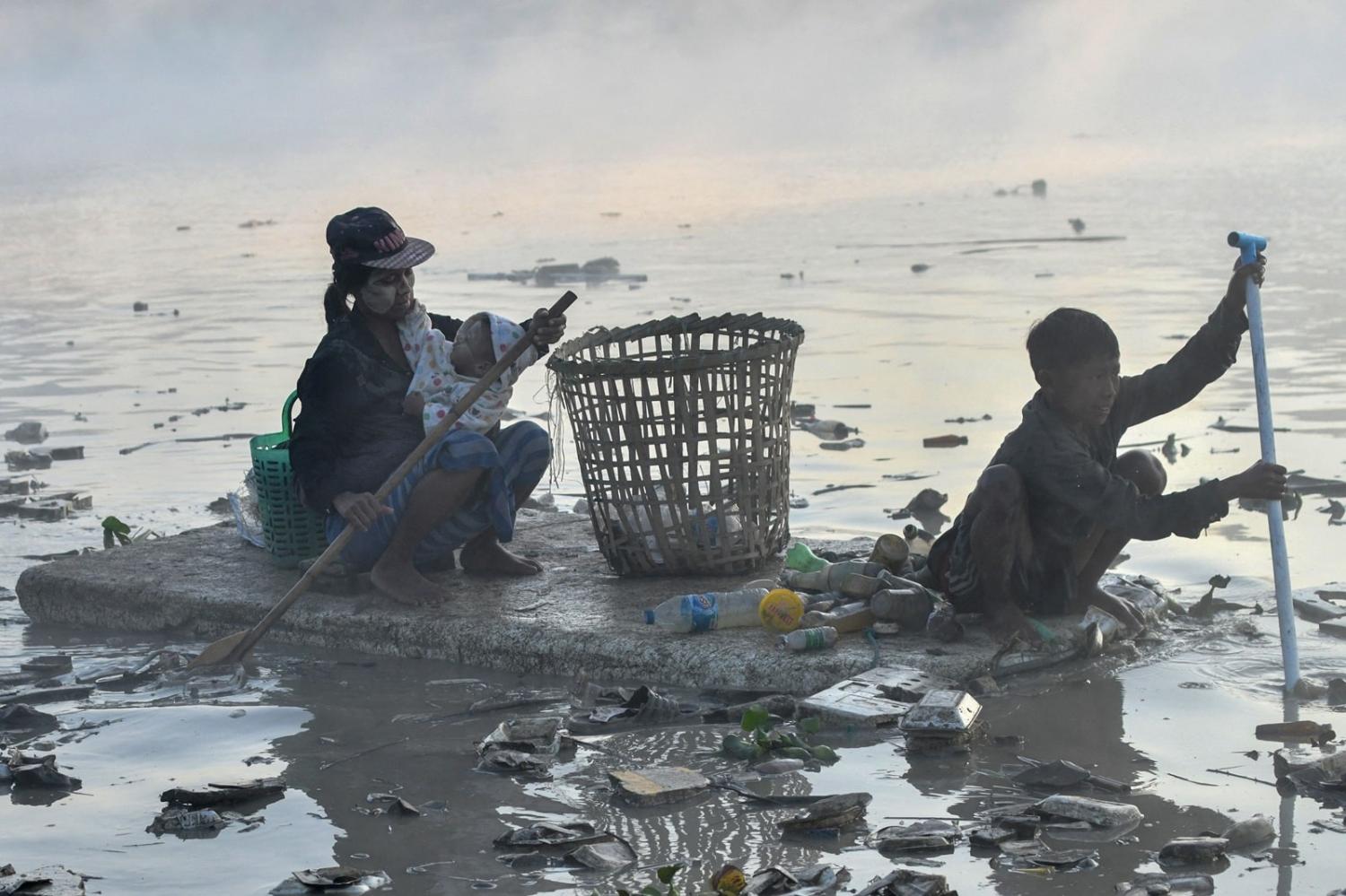 Myanmar waste collectors paddle a polystyrene boat in the murky waters of a Yangon creek after being driven to find work by a post-coup economic crisis, 14 January 2023 (Sai Aung Main/AFP via Getty Images)