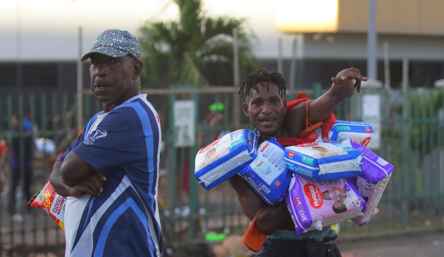 Men carry looted goods amid a state of unrest in Port Moresby on 10 January 2024 (AFP via Getty Images)