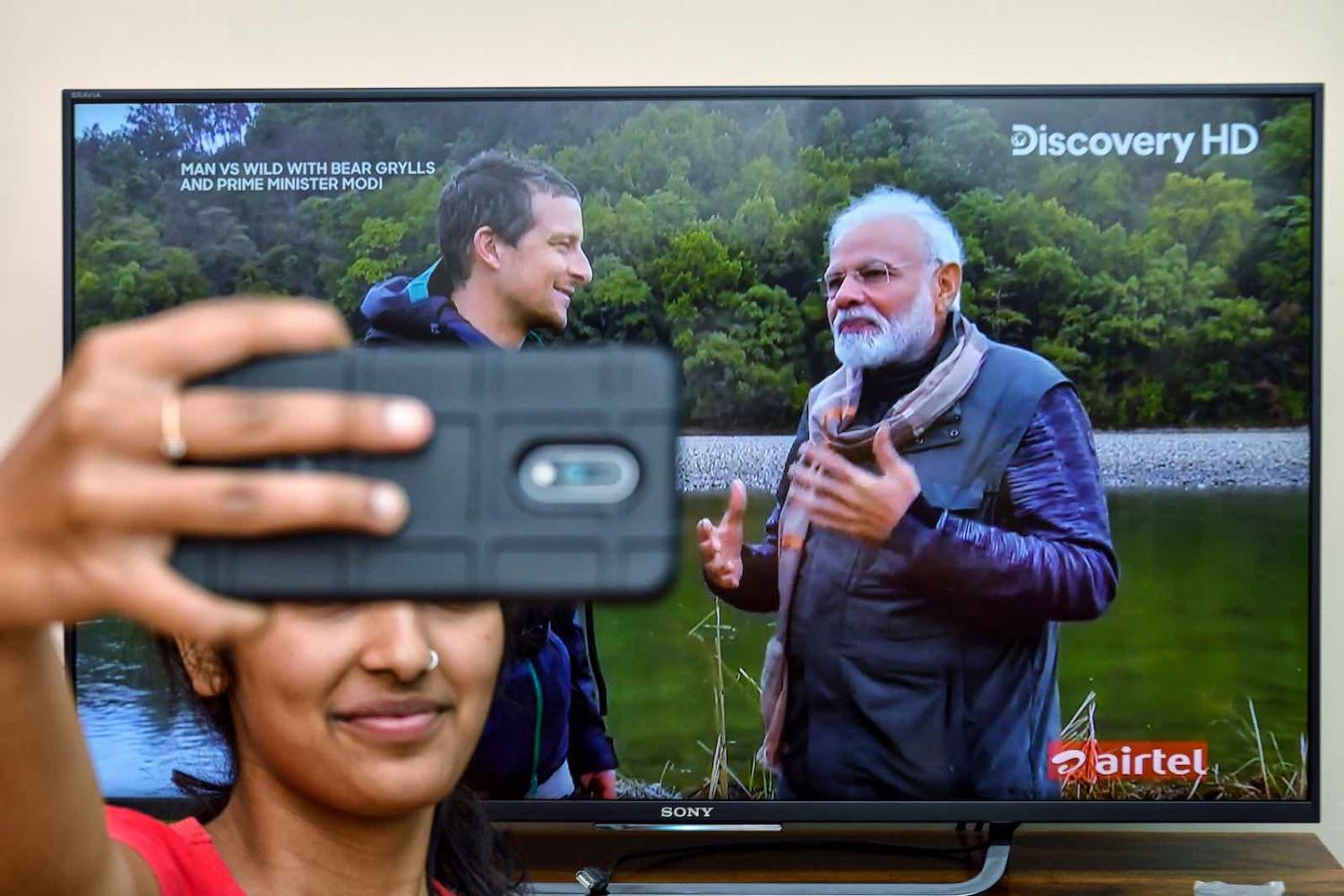 A fan in Bangalore snaps a selfie with the televised image of PM Modi (r) and Grylls (Photo: Manjunath Kiran via Getty)