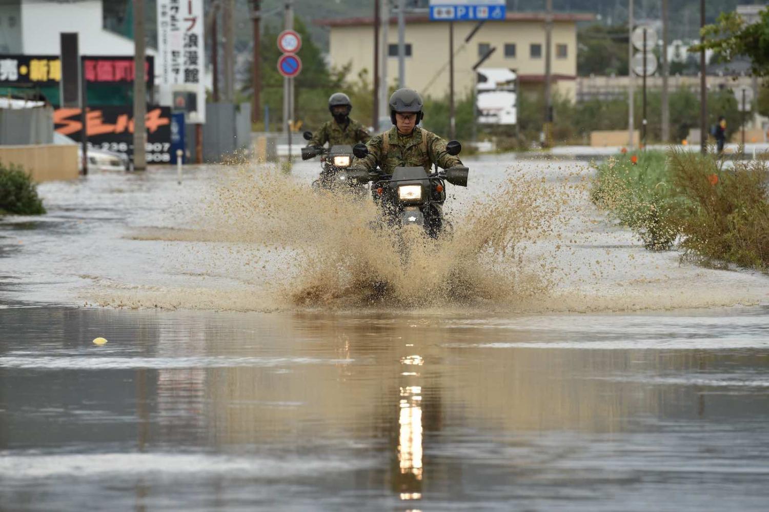 Military personnel drive their motorbikes down a flooded street in the aftermath of Typhoon Hagibis in Nagano on 14 October (Photo: Kazuhiro Nogi/AFP/Getty Images)