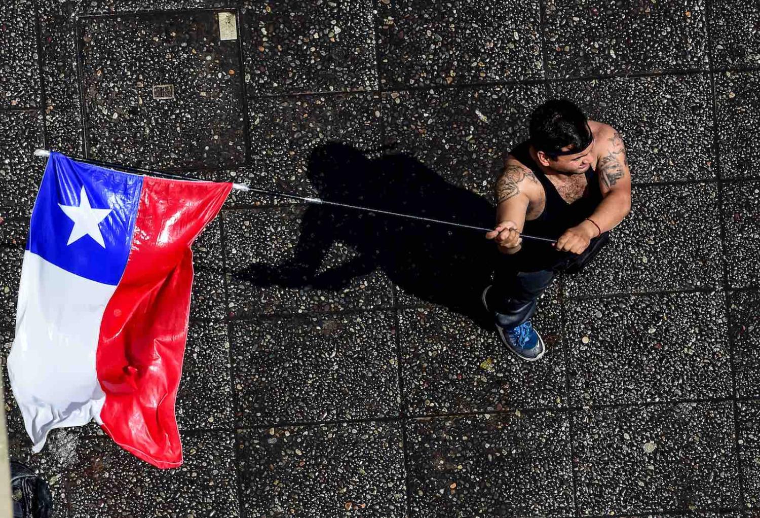 A demonstrator waves the Chilean national flag during a protest in Santiago, 20 October 2019 (Photo: Martin Bernetti/AFP/Getty)
