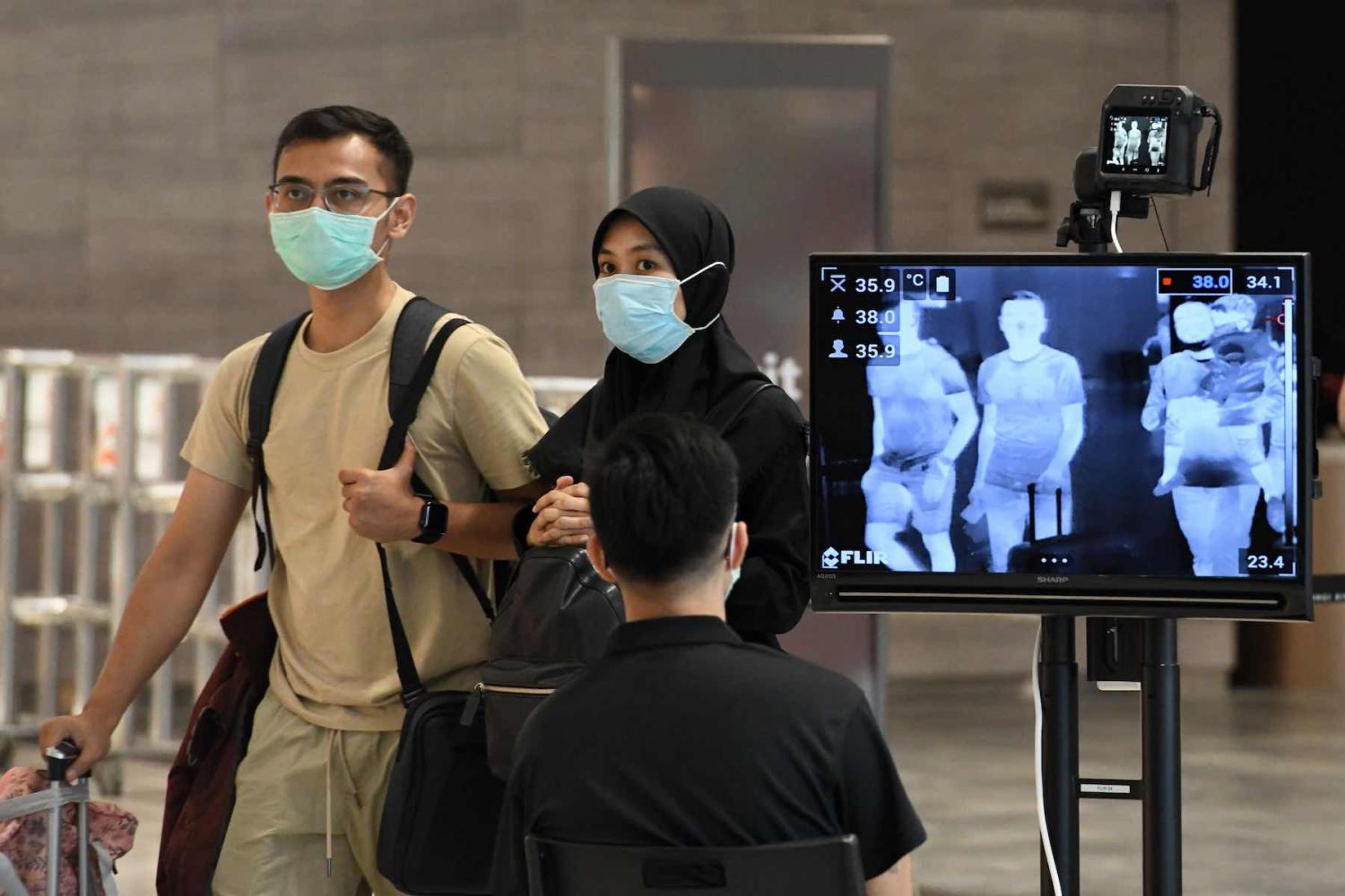 A couple walking past a temperature screening check at Changi International Airport in Singapore, 27 February 2020 (Roslan Rahman/AFP via Getty Images)