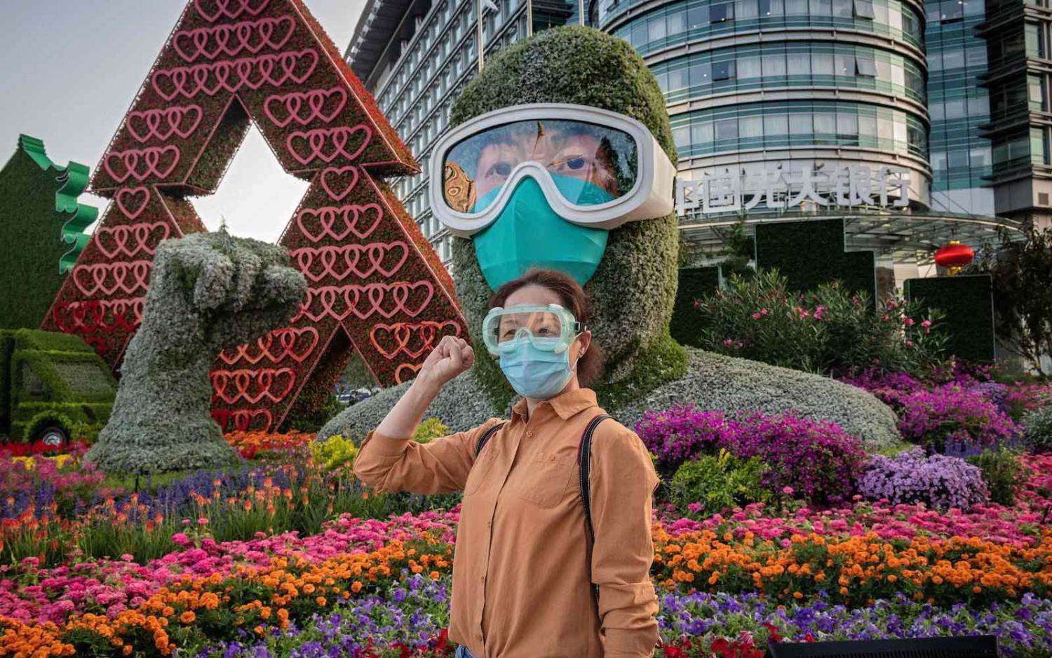 A woman poses in front of a flower display dedicated to frontline healthcare workers during the Covid-19 pandemic, Beijing, 29 September 2020 (Nicolas Asfouri/AFP via Getty Images)