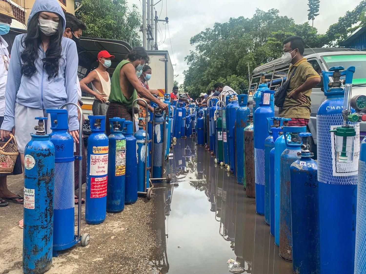 People stand with empty oxygen canisters as they wait to fill them up outside a factory in Yangon on 11 July (Ye Aung Thu/AFP via Getty Images)