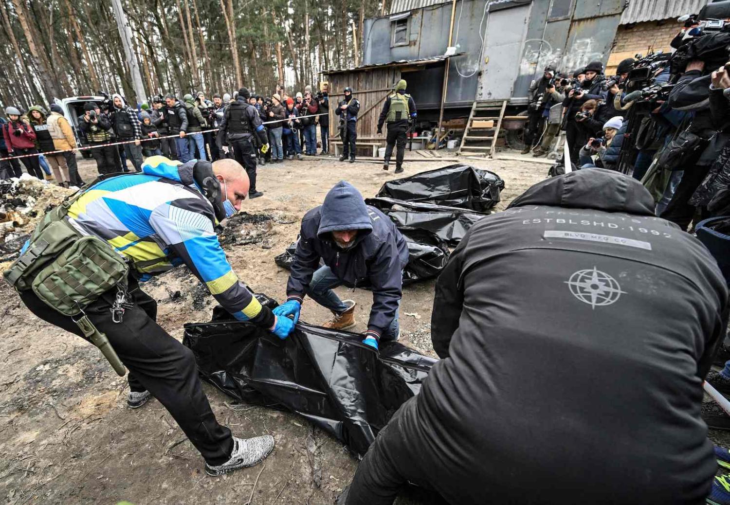 Journalists lined up against a taped off area while human remains are lifted into body bags in the Ukrainian town of Bucha on 5 April (Genya SAVILOV/AFP via Getty Images)