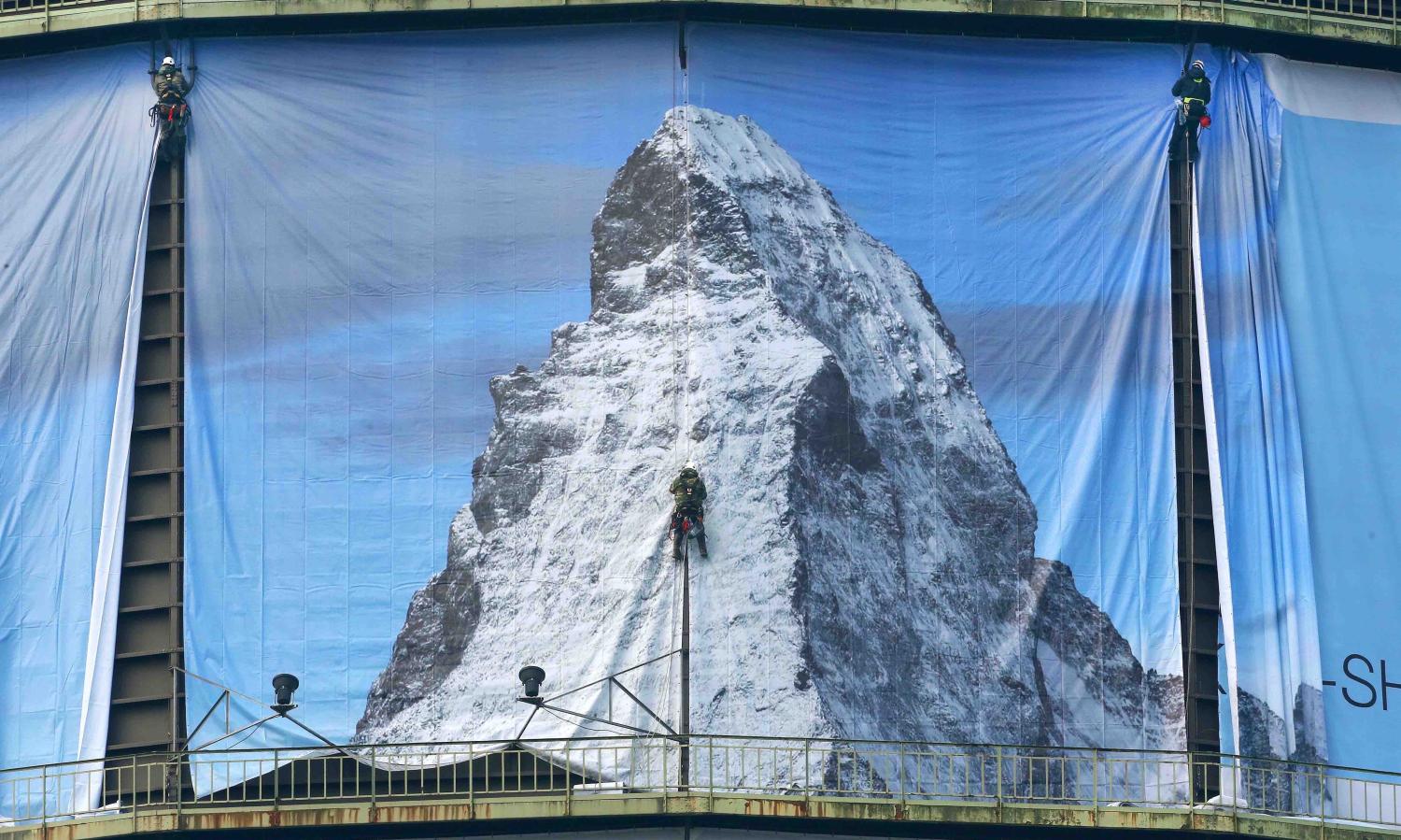 Workers hang a 1400 square-metre banner to promote the exhibition “The Call of the Mountains” on 2 March (Roland Weihrauch/Getty)
