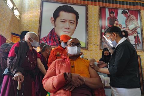 A Buddhist monk is vaccinated last month sitting in front of a portrait of Bhutan’s King Jigme Khesar Namgyel Wangchuck (Upasana Dahal/AFP via Getty Images)